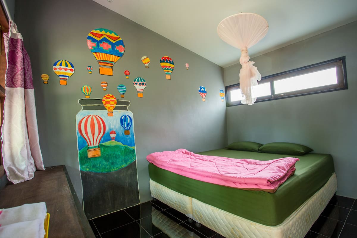 A bedroom with a green bed, a pink blanket, and a wall decorated with colorful hot air balloon stickers.