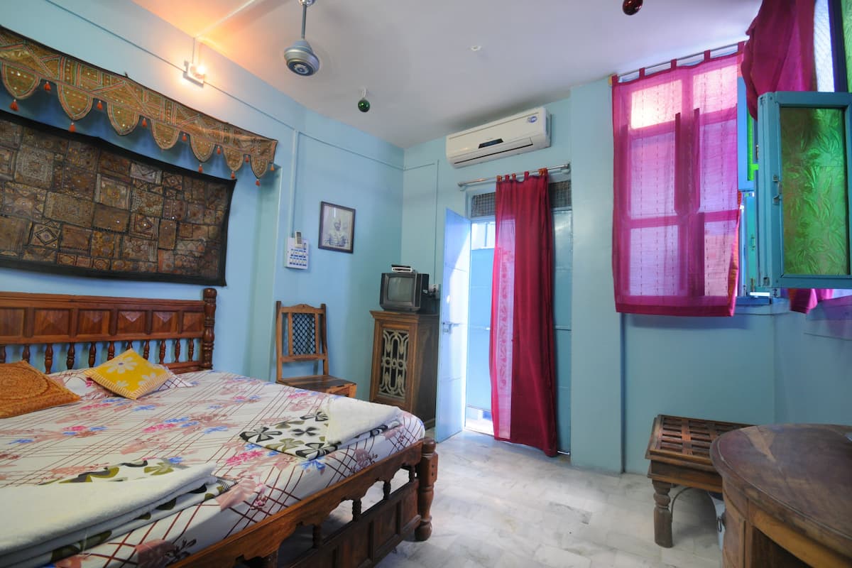 A bedroom with a wooden bed, a television, an air conditioner, and a window with a red curtain.