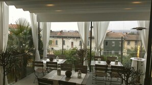 An outdoor dining area with tables and chairs, white curtains, and a view of buildings in the background. - La corte sul naviglio (Boffalora Sopra Ticino)