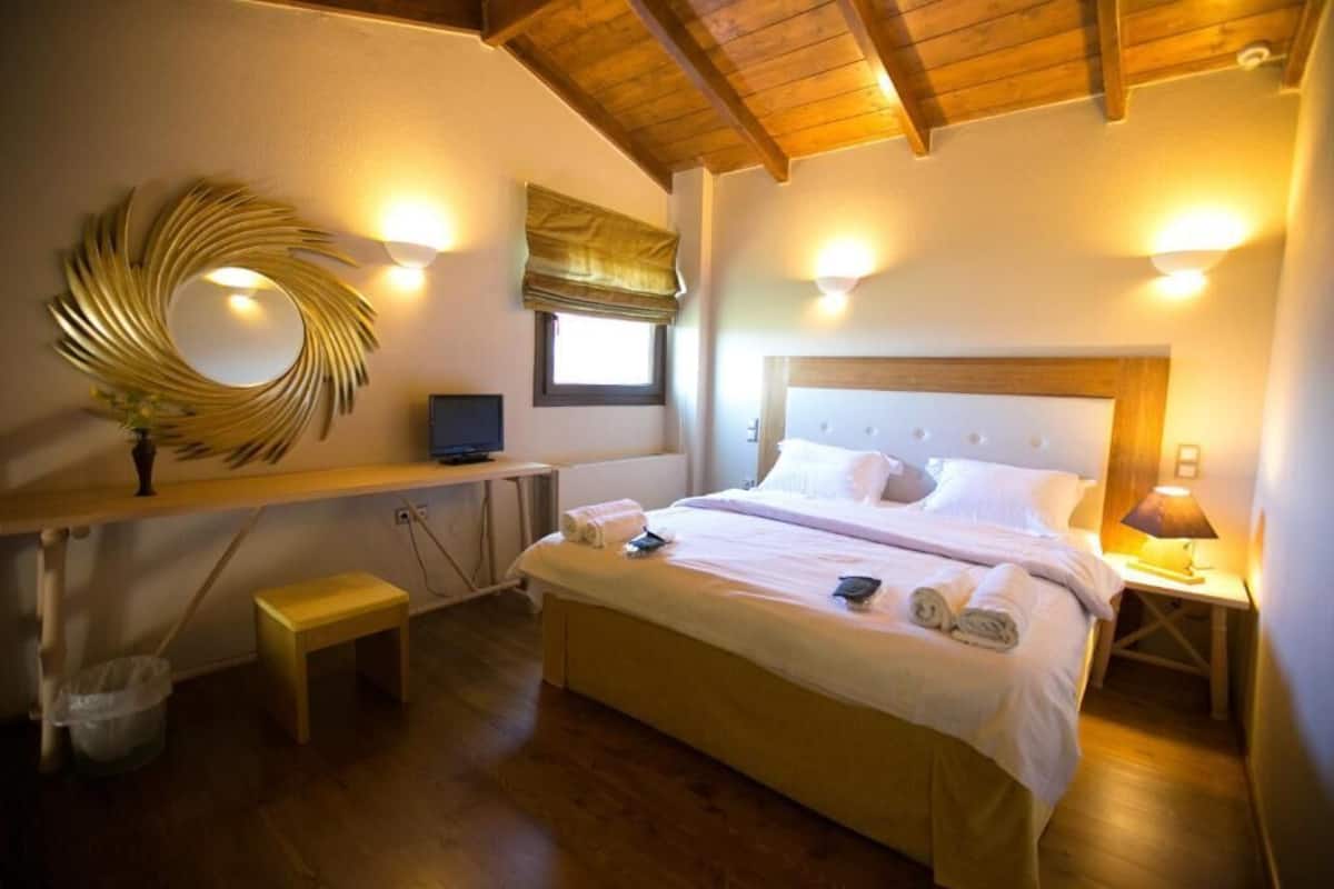 Une chambre avec un plafond en bois, un lit recouvert de draps blancs, une table de chevet avec une lampe et un miroir fixé au mur.