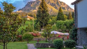 A garden with a stone wall, a pathway, and a building with a mountain in the background. - Anavasi Mountain Resort (North Tzoumerka)