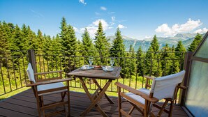 A wooden deck with a table and chairs, overlooking a forest and mountains. - Anavasi Mountain Resort (North Tzoumerka)