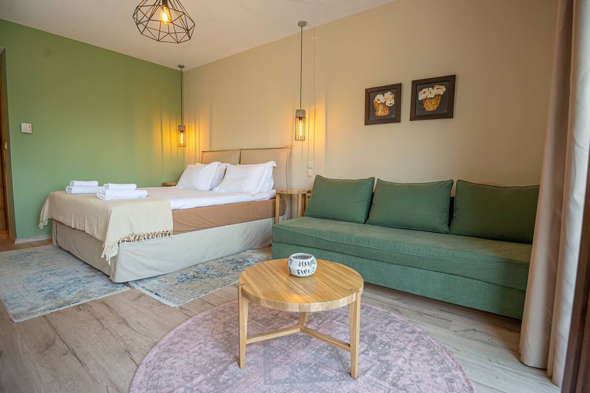 Une chambre à coucher avec un lit, un canapé vert, une table basse en bois et deux lampes fixées au mur.