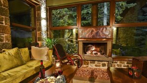 A cozy living room with a stone fireplace, large windows, and a dining area set for a meal. - Anavasi Mountain Resort (North Tzoumerka)