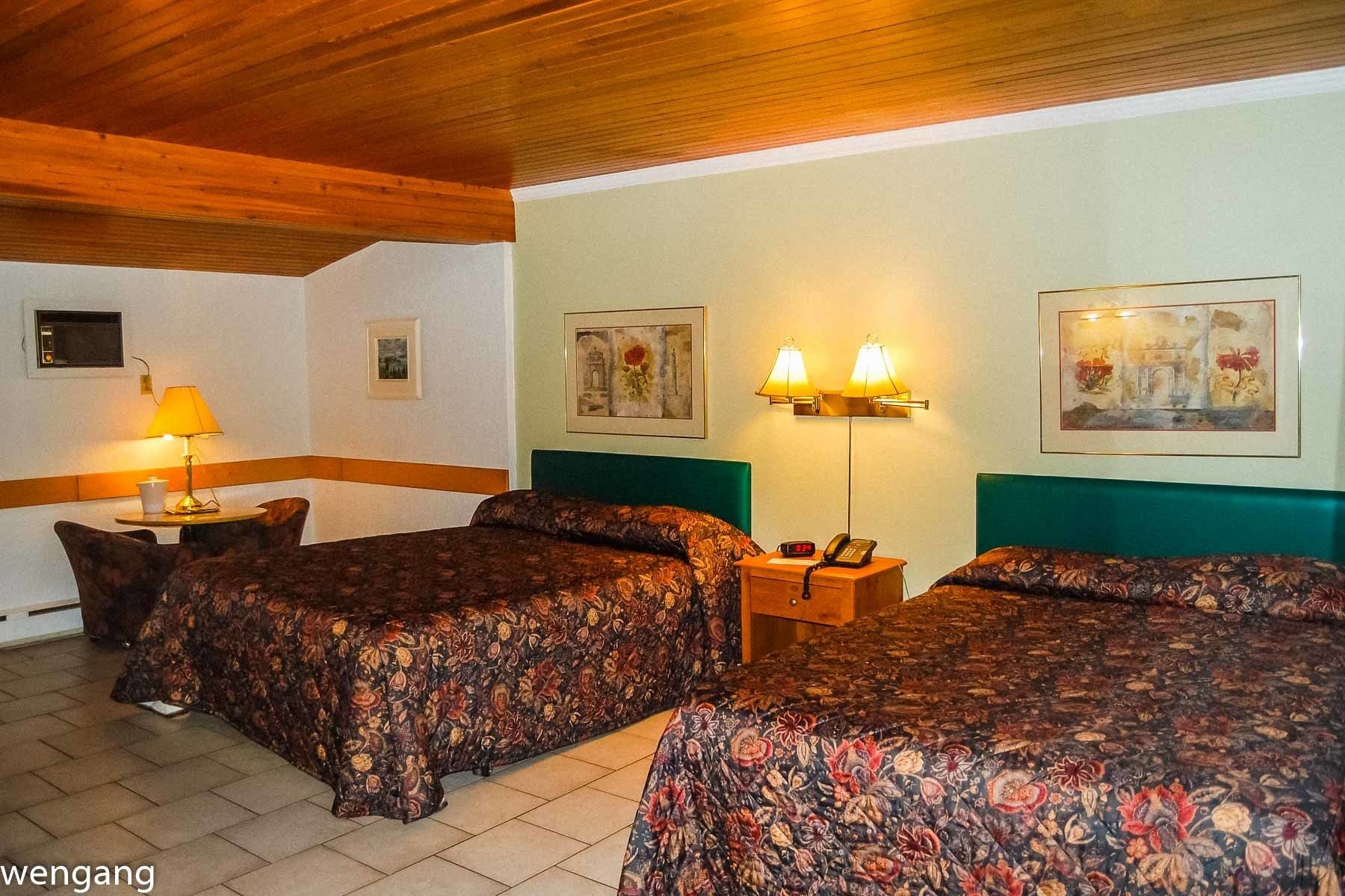 A hotel room with two beds, a nightstand with a lamp, and framed artwork on the walls.