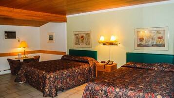A hotel room with two beds, a nightstand with a lamp, and framed artwork on the walls.