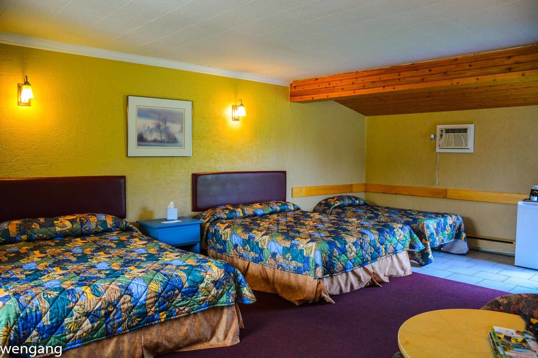 A hotel room with two beds, a purple rug, a wooden ceiling, and a painting on the wall.