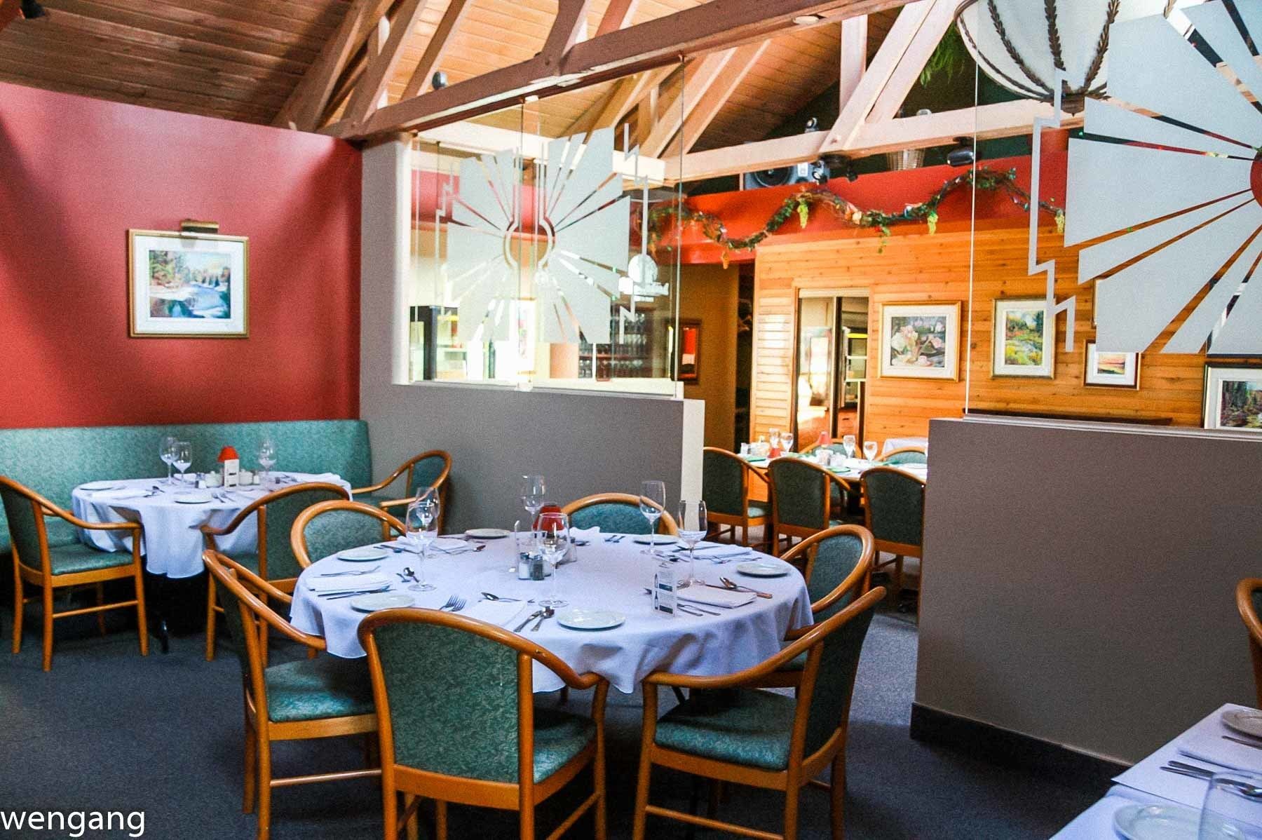 A restaurant with round tables, green upholstered chairs, and wooden beams on the ceiling.