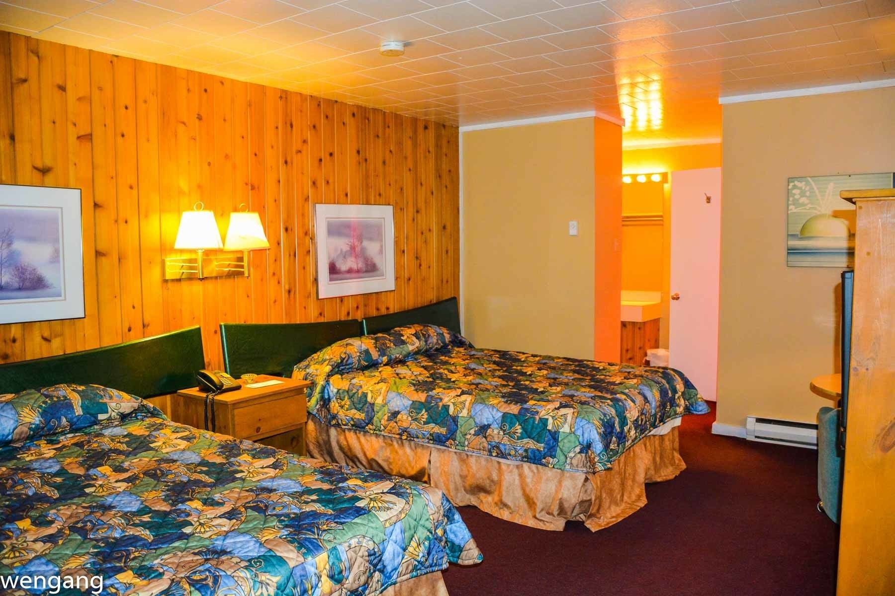 Habitación de hotel con dos camas, paredes de madera y una puerta que da a un baño.
