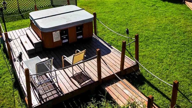 A hot tub on a wooden deck with a view of a grassy area and a building in the background.
