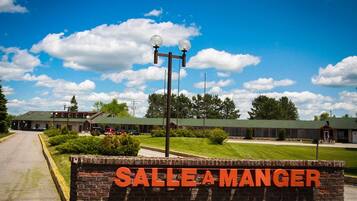 A brick wall with the words "SALLE A MANGER" in bold letters, a street lamp, and a building with a green roof in the background.