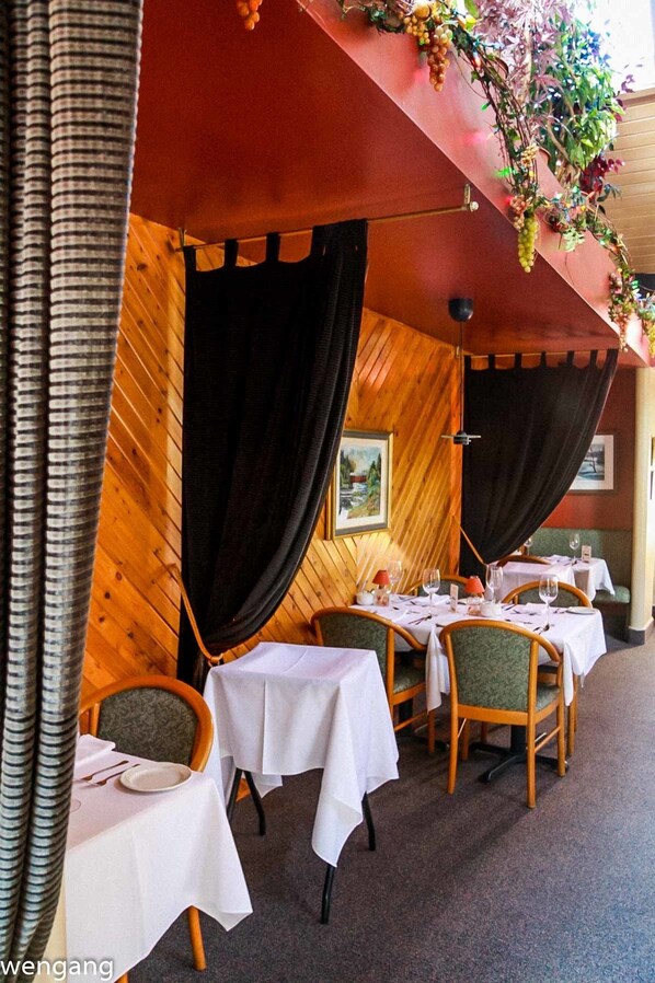 An outdoor dining area with wooden walls, black curtains, and tables set for dining. - Auberge Motel Godard (Nominingue)