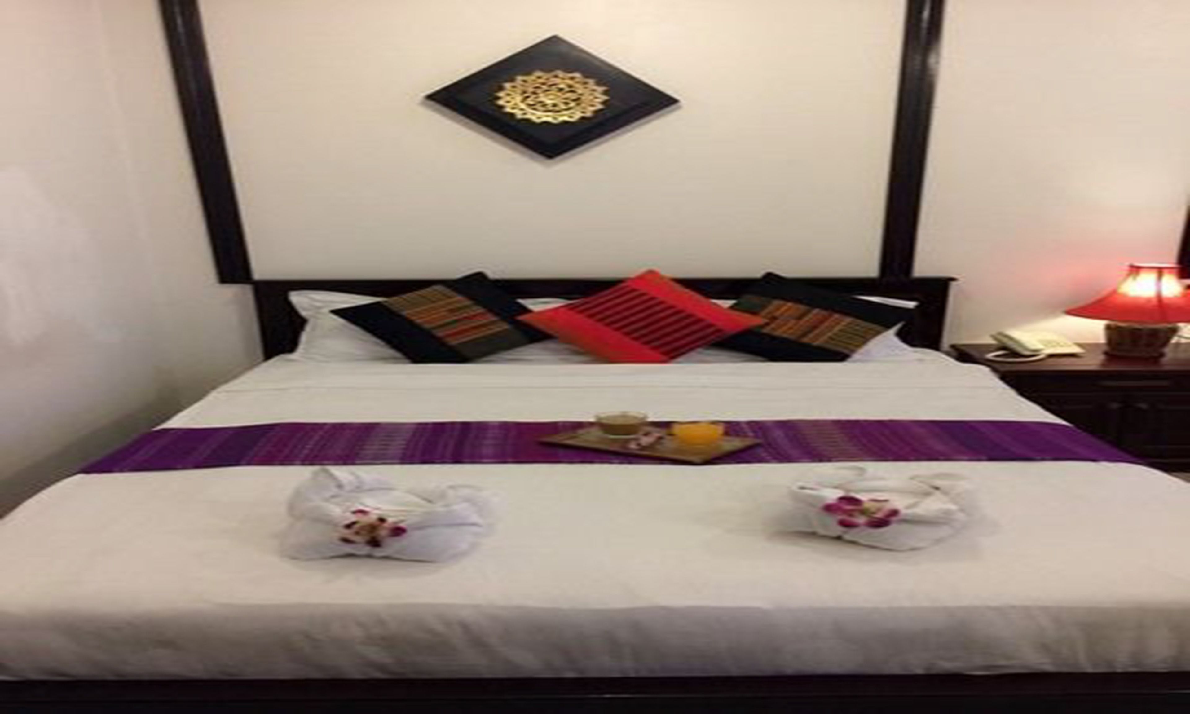 A neatly made bed with a purple bedspread, two towels, and a tray with a drink and snacks.