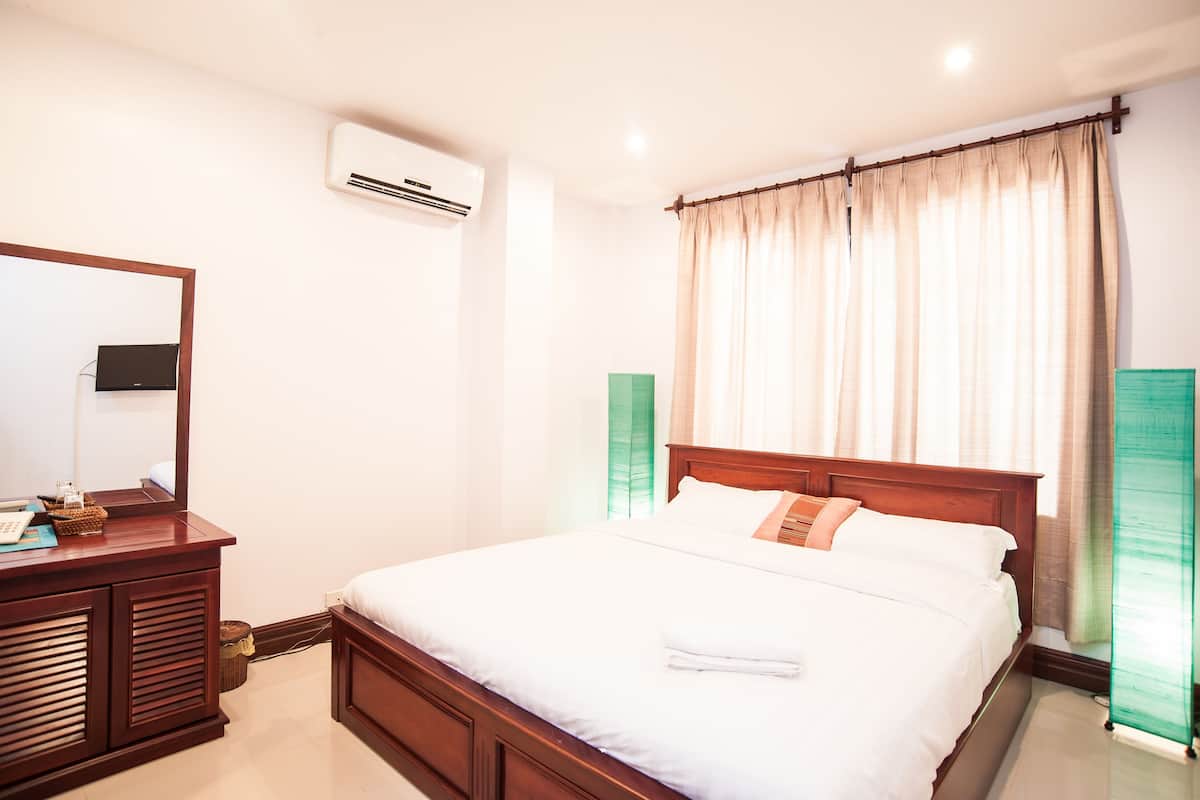 Uma cama bem arrumada com lençóis brancos, cabeceira de madeira e mesa de cabeceira com um espelho e um pequeno objeto decorativo.