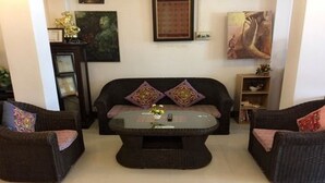 A living room with a dark brown sofa, two armchairs, a glass coffee table, and decorative pillows. - Vientiane SP Hotel (Vientiane)