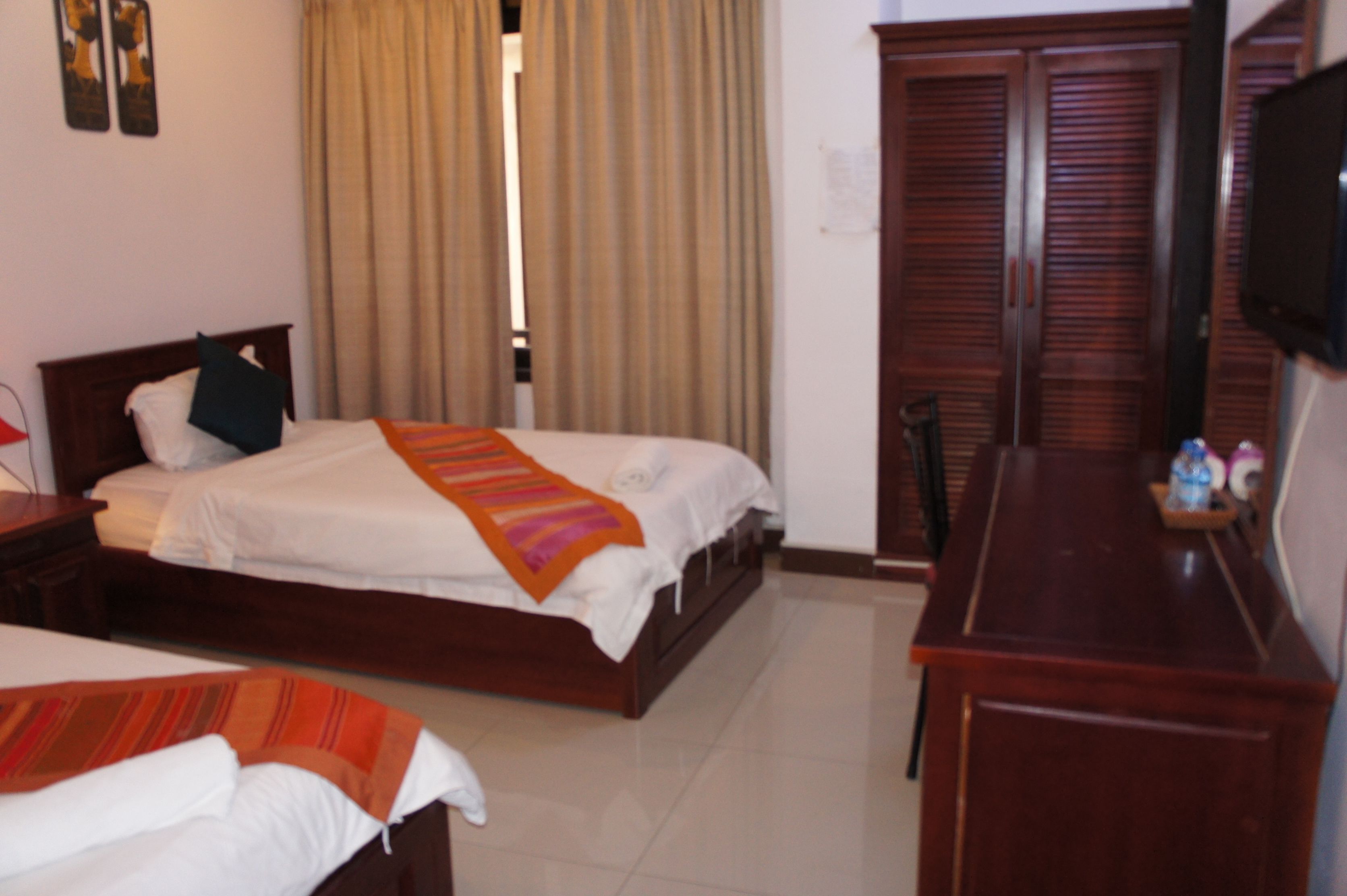 A hotel room with two beds, a wooden desk, a television, and a wardrobe.