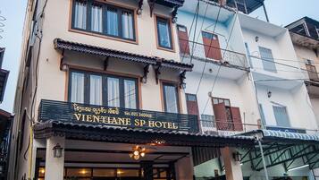 Traditional architecture meets modern charm at the Vientiane Sp Hotel, featuring a grand entrance with potted plants and classic wooden shutters.