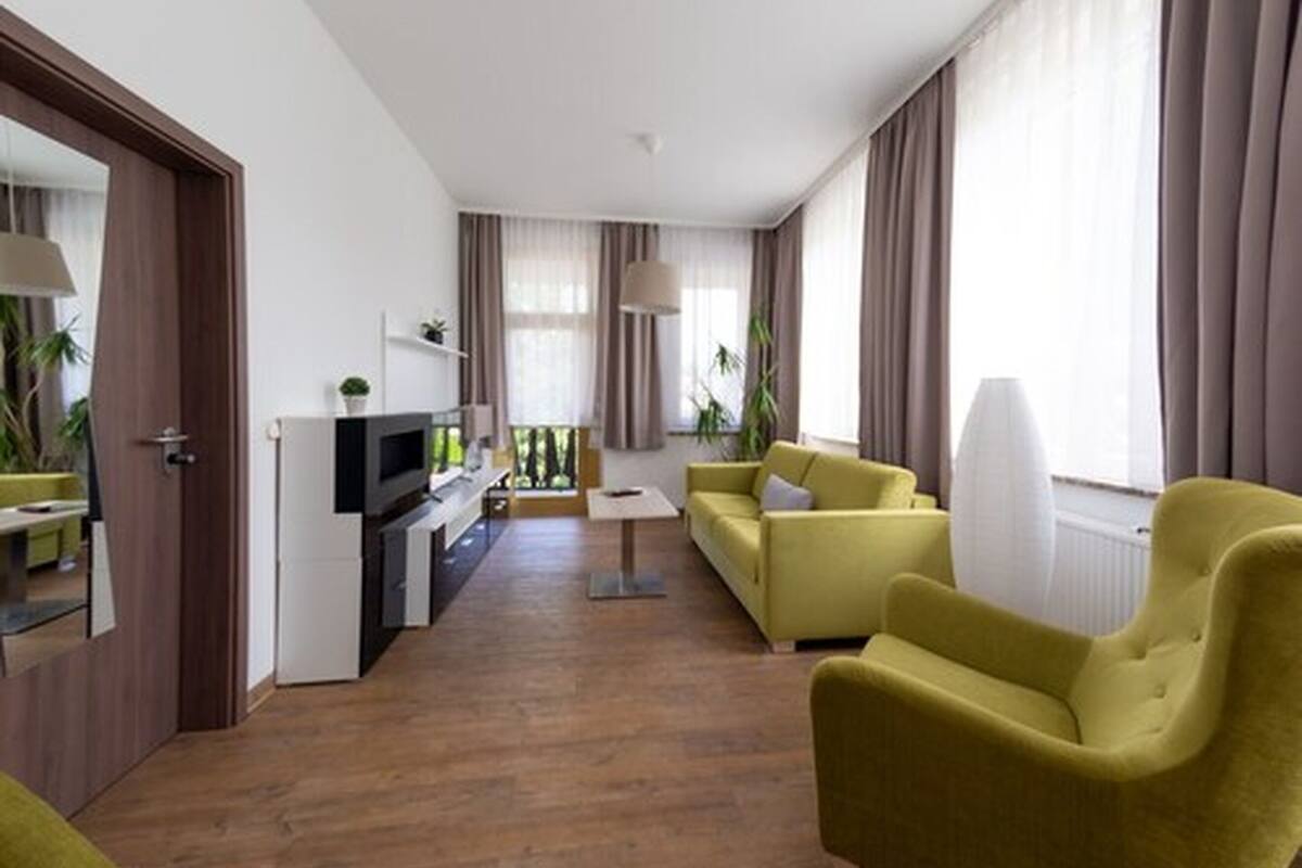 Una sala de estar moderna con un sofá amarillo, un televisor y un comedor con mesa y sillas.