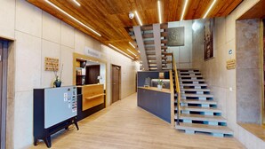 Een receptie met een houten receptiebalie, een trap met een bijzonder ontwerp, en bewegwijzering naar voorzieningen.
