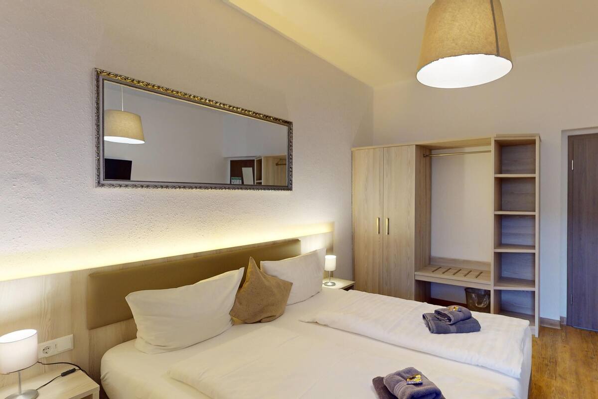 Habitación de hotel con cama, lámparas de noche, espejo, armario y escritorio con silla.