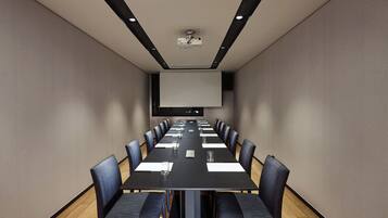A conference room with a long table, chairs, a projector, and a screen.