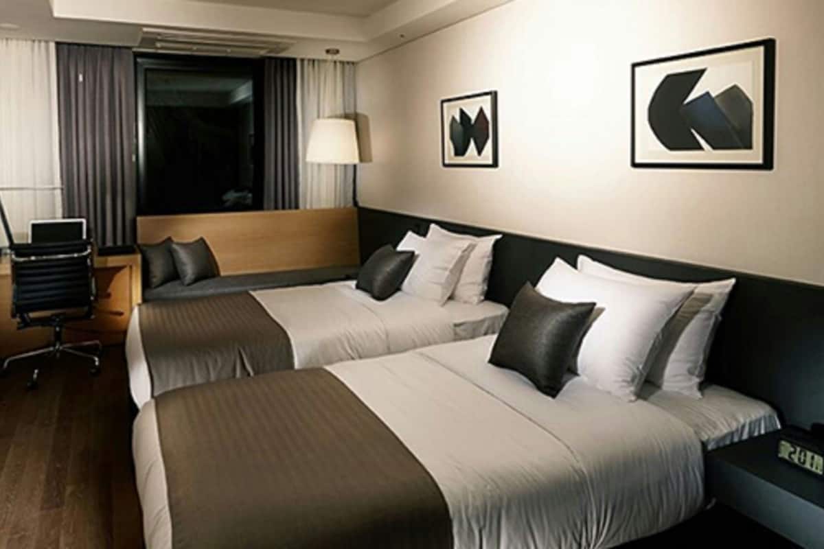A hotel room with two beds, a desk, a chair, a lamp, and a TV.