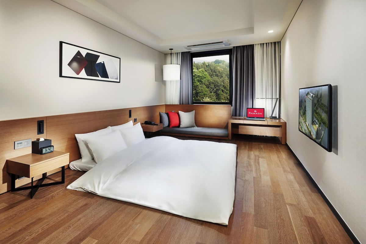 A hotel room with a bed, bedside table, lamp, and a window with curtains.