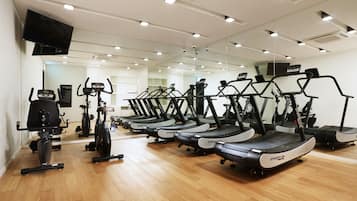 Un gimnasio con cintas de correr, bicicletas estáticas y una pantalla de televisión.