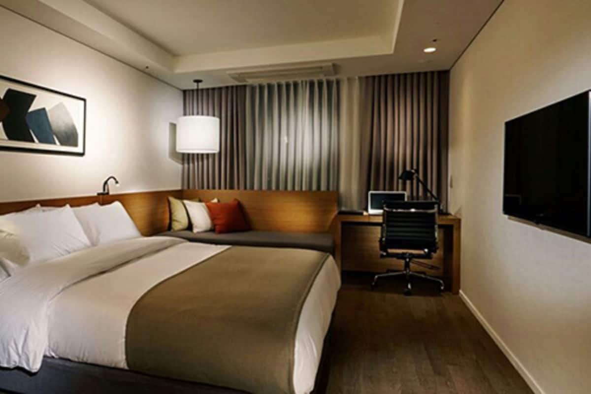 A hotel room with a bed, a desk, a chair, a TV, and a window with curtains.