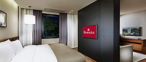 A modern hotel room with a large bed, a TV, and a sign reading "RAMADA".