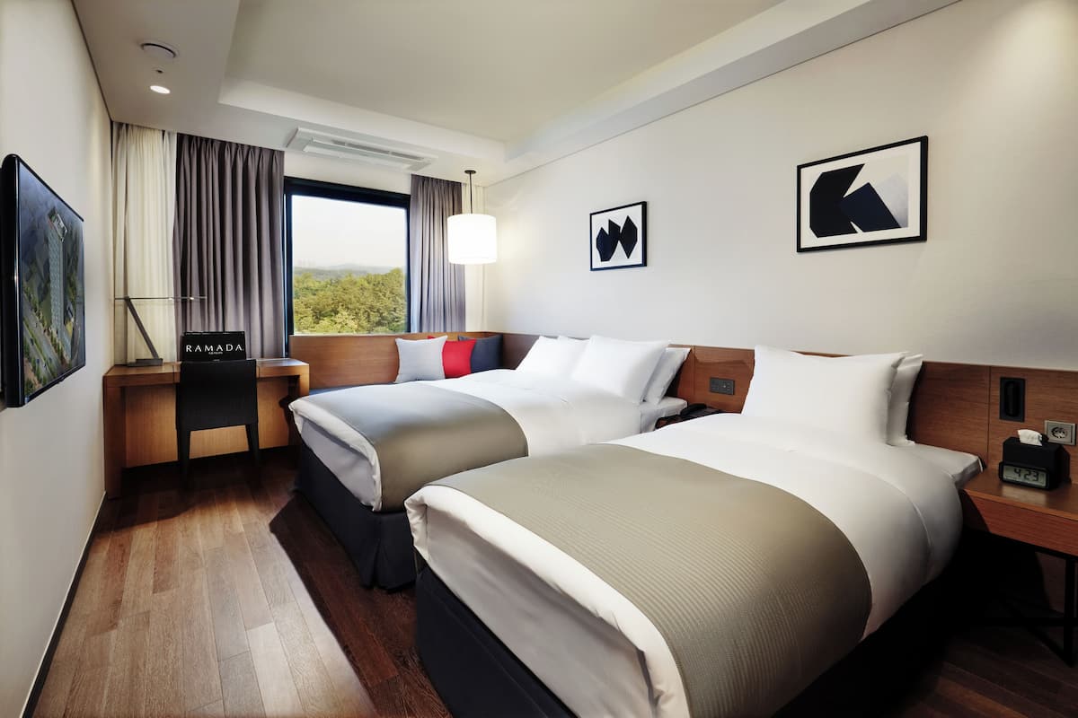 A hotel room with two beds, a desk, a chair, and a window with curtains.