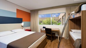 Una habitación de hotel con cama, escritorio, silla y literas.