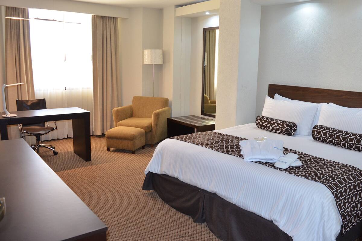 Ein Hotelzimmer mit Bett, Schreibtisch, Stuhl, Lampe und Spiegel.
