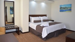 A hotel room with a large bed, a bedside table, a chair, a mirror, and a painting on the wall.