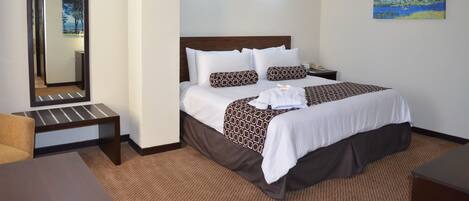 Habitación de hotel con una cama grande, una mesita de noche, una silla, un espejo y un cuadro en la pared.