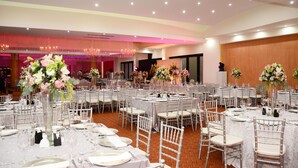 A banquet hall with round tables, white chairs, and floral centerpieces.