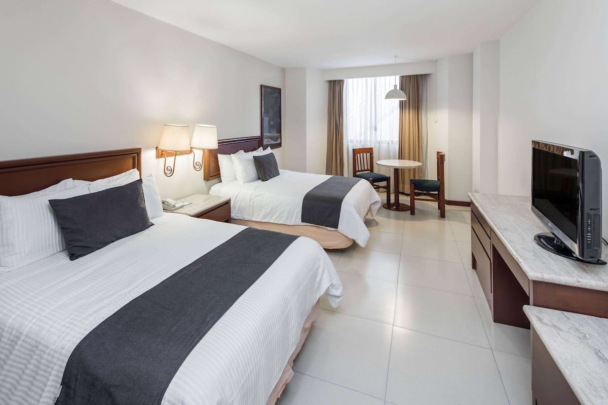 Ein Hotelzimmer mit zwei Betten, einem Schreibtisch mit Fernseher, einem Sessel und einem kleinen Tisch.