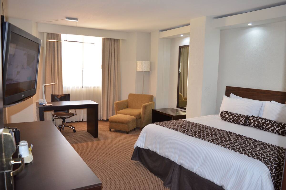 Ein Hotelzimmer mit Bett, Schreibtisch, Stuhl, Fernseher und Lampe.