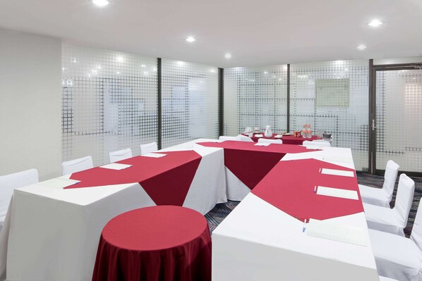 A conference room with white and red tables, white chairs, and a glass partition with a grid pattern.
