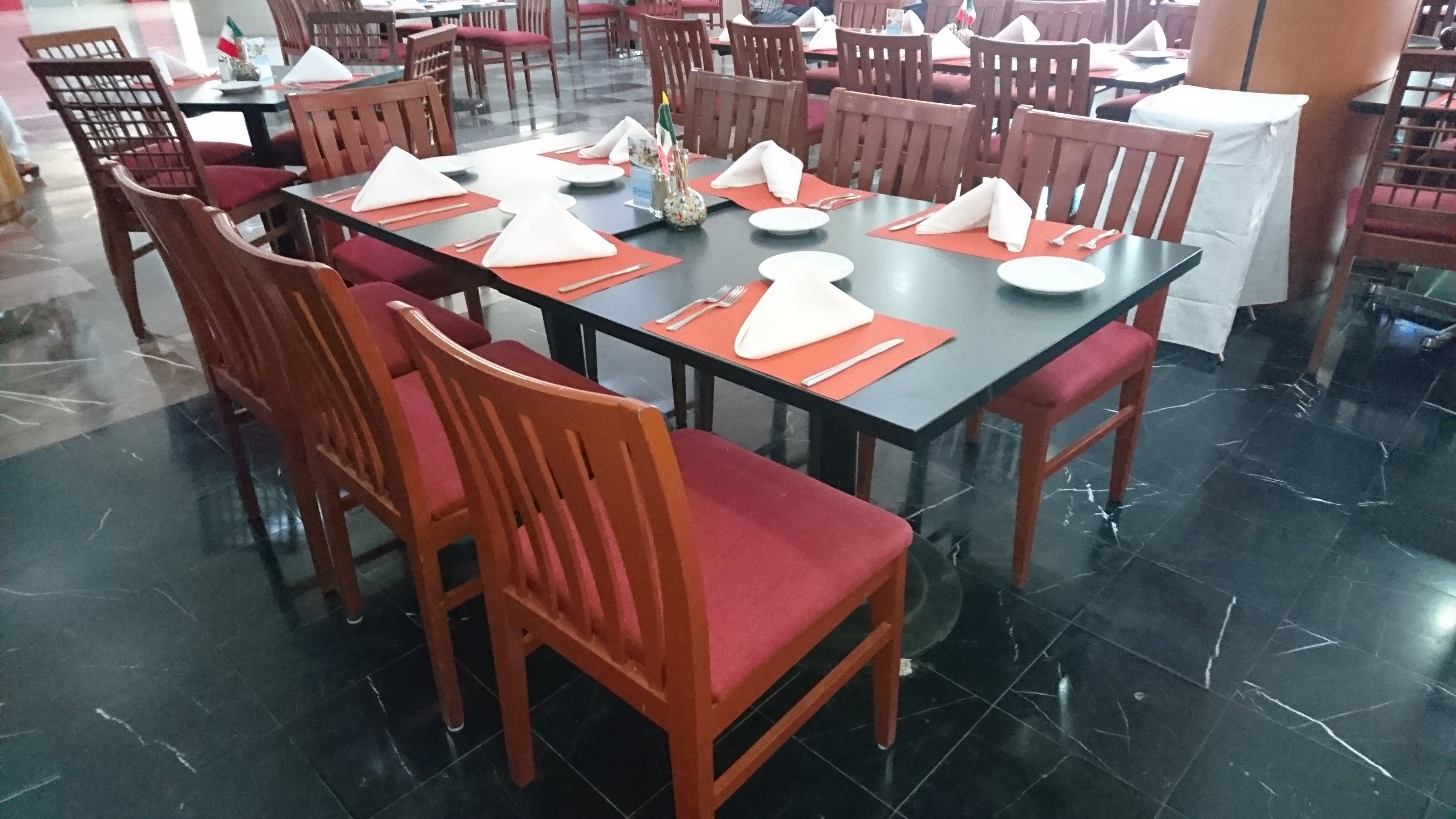Comedor con mesas dispuestas para varias personas, sillas y piso de baldosas.
