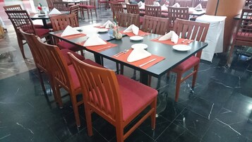 Comedor con mesas dispuestas para varias personas, sillas y piso de baldosas.