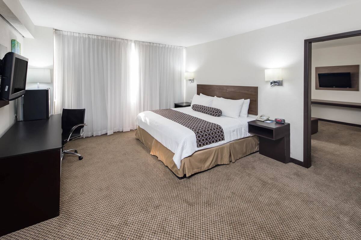 Ein Hotelzimmer mit einem großen Bett, einem Schreibtisch, einem Sessel, einem Fernseher und einem Spiegel.