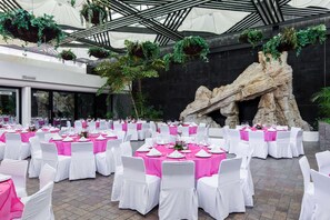 A banquet hall with round tables set for events, featuring white chairs and pink tablecloths.