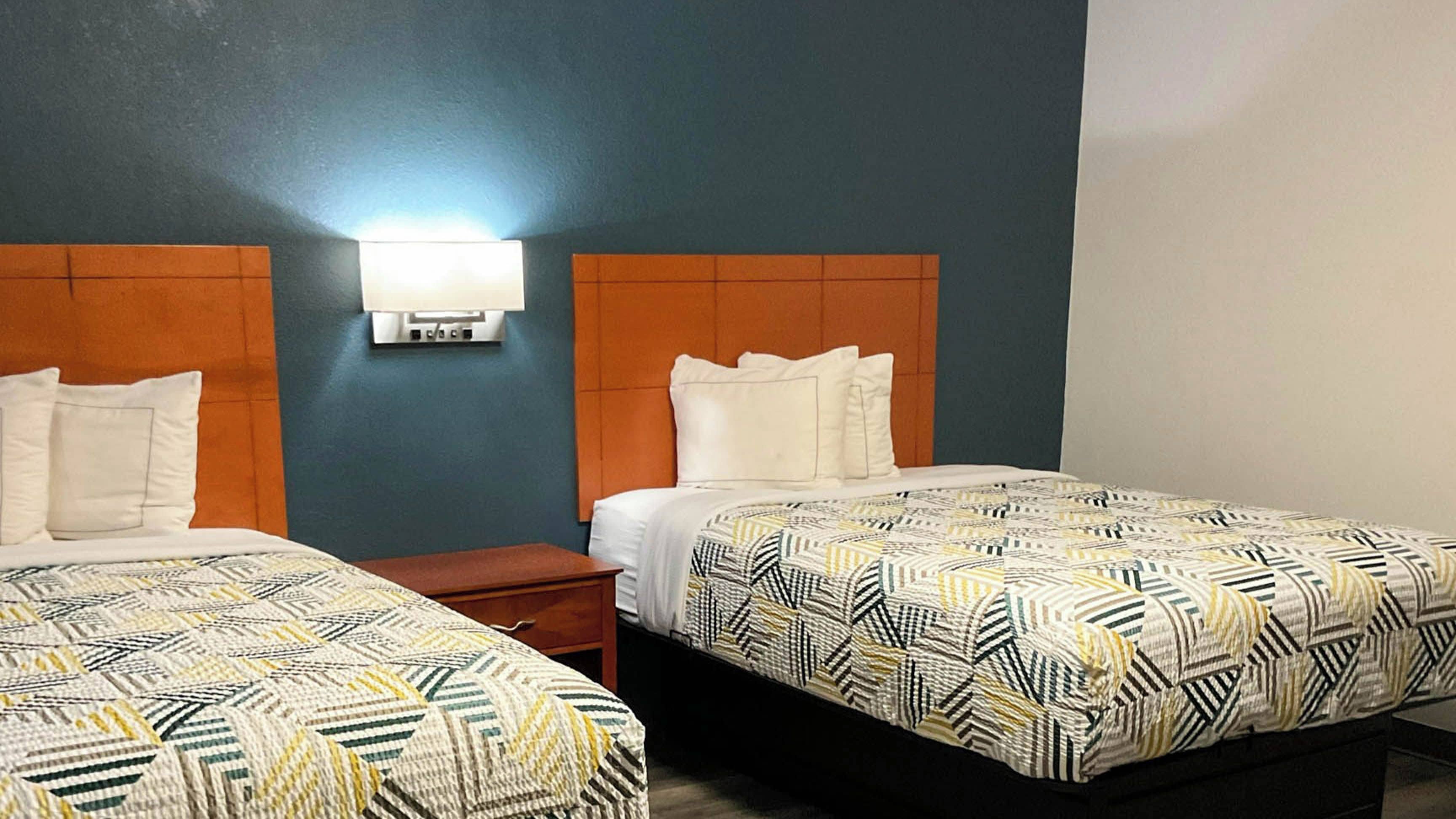 Ein Hotelzimmer mit zwei Betten, jeweils mit einem gemusterten Überwurf, einem Nachttisch und einer Wandlampe.
