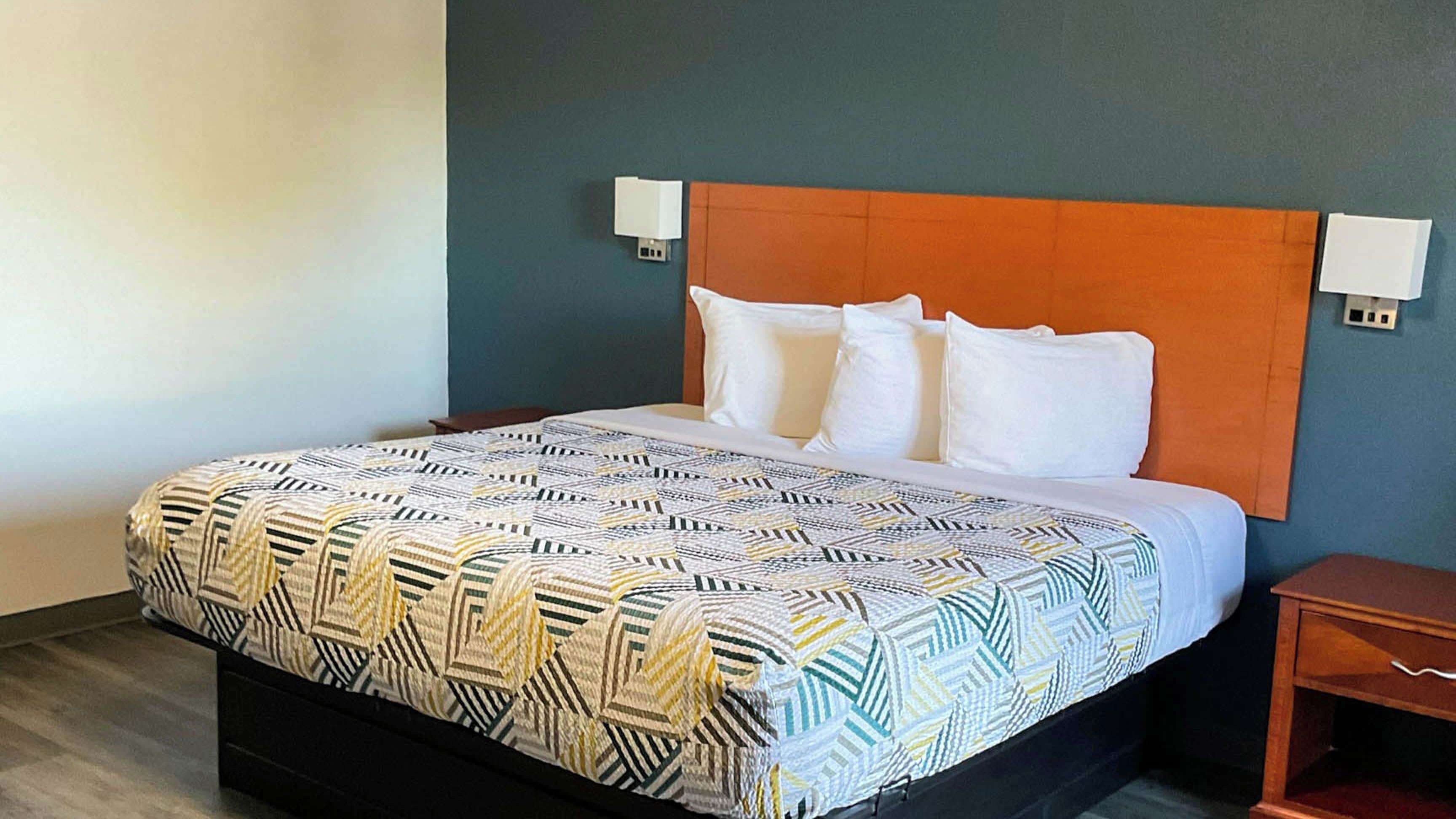 Habitació d'hotel amb llit, una tauleta de nit i dues làmpades penjades a la paret.