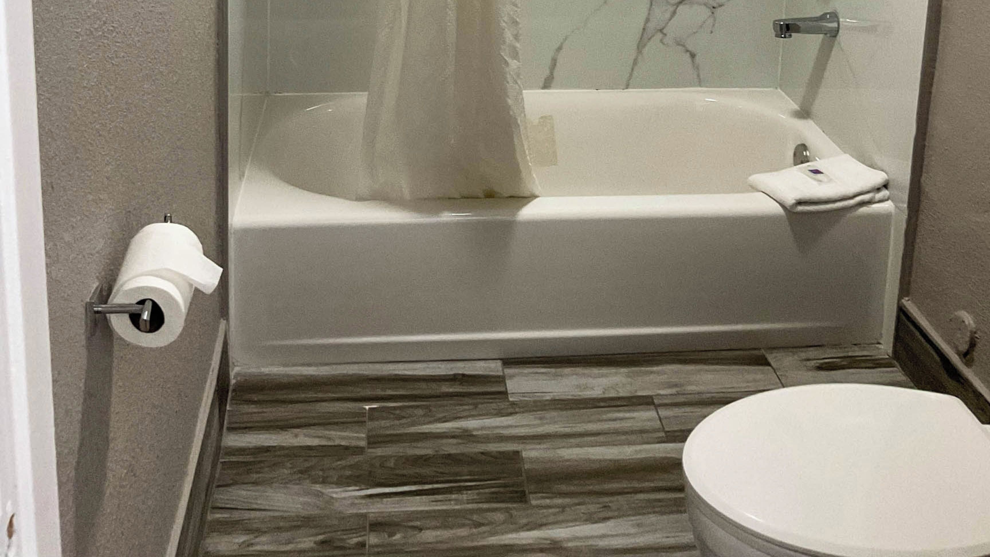 A bathroom with a bathtub, toilet, and a roll of toilet paper on the wall.