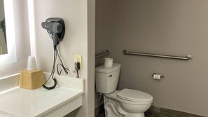 A bathroom with a toilet, a hand dryer, a towel dispenser, and a hand sanitizer on the counter. - Studio 6 Suites Hot Springs, AR (Hot Springs)