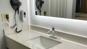 A bathroom with a sink, a mirror, and a hairdryer mounted on the wall. - Studio 6 Suites Hot Springs, AR (Hot Springs)