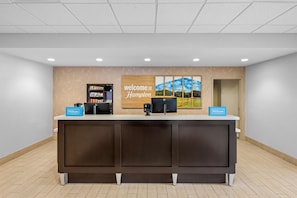 A reception desk with a 'Welcome to Hampton' sign, a minibar, and a 'Hilton Honors' sign.