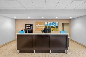 Mostrador de recepción con un cartel de 'Welcome to Hampton', una minibar y un cartel de 'Hilton Honors'.